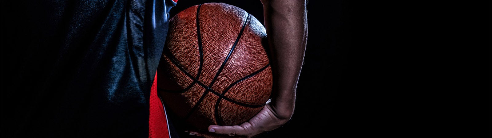 Close-up of a person holding a basketball against a dark background